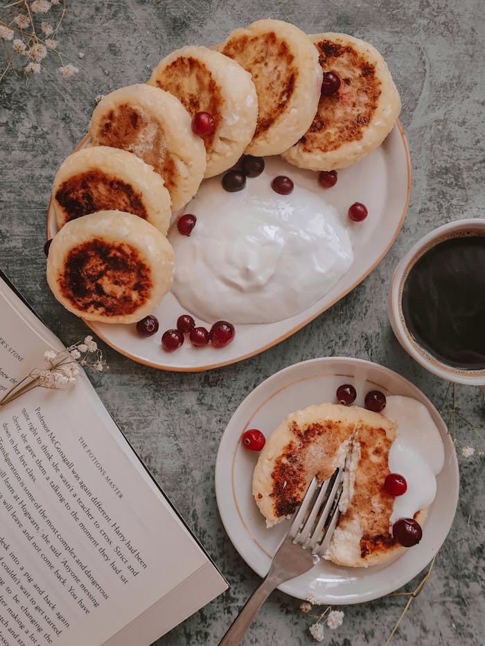 Cozy breakfast scene featuring traditional syrniki with cranberries, yogurt, and a hot cup of coffee.